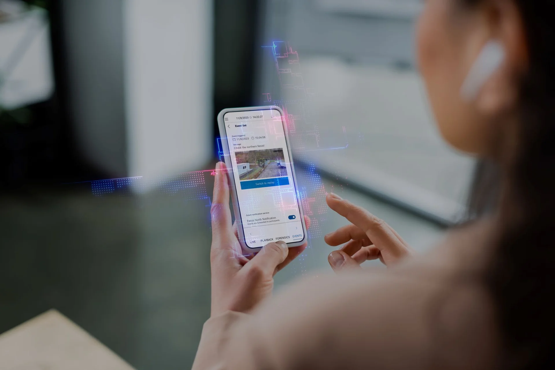 A person interacts with a smartphone showing the VideoView+ surveillance app, featuring a video thumbnail and event notification settings.